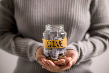 Woman holding coins and cash in jar with words Give or Donate elegantly lettered on its front, embodying spirit of giving. words, lettering, donate, jar, money, giving, woman, give, coin.の写真素材