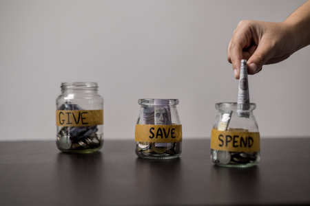 Give, Save, Spend money jars. She organized her finances into three jars labeled Give, Save and Spend, ensuring a balanced approach to managing her money. words, lettering, donate, jar, money.の写真素材