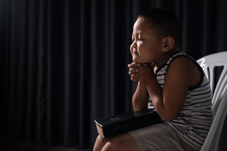 A little boy, full of faith, sits with the holy Bible in his hands, praying to God and embracing his Christian religion. child, person, bible, boy, religion, christian, holy, little, faith, god.の写真素材