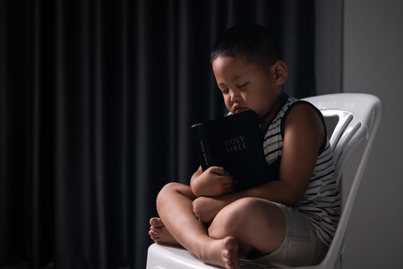 A little boy, full of faith, sits with the holy Bible in his hands, praying to God and embracing his Christian religion. child, person, bible, boy, religion, christian, holy, little, faith, god.の写真素材