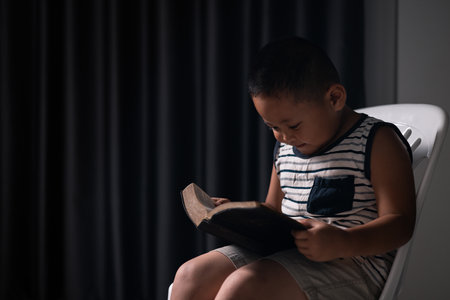 A little boy, full of faith, sits with the holy Bible in his hands, praying to God and embracing his Christian religion. child, person, bible, boy, religion, christian, holy, little, faith, god.の写真素材