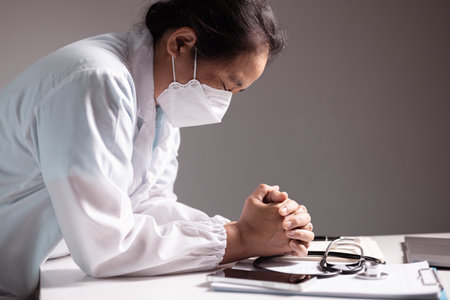 Woman prays with her hands clasped, believing in the care of doctors and medical professionals as she faces disease in a hospital or clinic, trusting in the strength of health care. doctor, disease.の写真素材