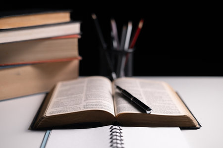 Old library, an open Bible lay on the table, its holy pages of scripture illuminated in the dark room. bible, holy, dark, old, open, library, pages, scripture, table, book, page.の写真素材