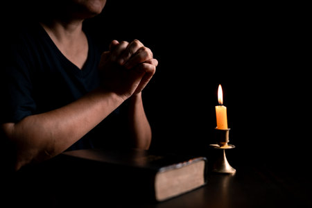 In the dark, hand clasped in prayer, illuminated by the soft candlelight, as black flames of candle fire flickered gently. candle, pray, hand, prayer, black, fire, flames, candlelight, light, dark.の写真素材