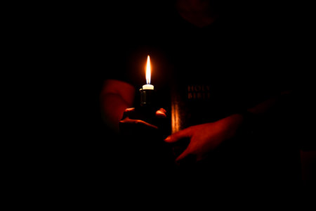 In the church, candle flickered beside cross as Christians gathered to pray, their faith in Jesus and spiritual devotion illuminated by Bible in background, deepening their Catholic worship.の写真素材