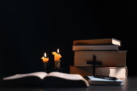 Dark, an antique candle cast its light on the old Bible, its flames flickering gently over the book on the table, symbolizing the enduring essence of religion. candle, bible, dark, light, book, old.の写真素材