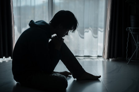 Silhouette of lost cast long shadow, embodying deep despair and hopelessness left him feeling perpetually stressed, sad, and unhappy. man sat alone, feeling weight of anxiety, stress, and depression.の写真素材