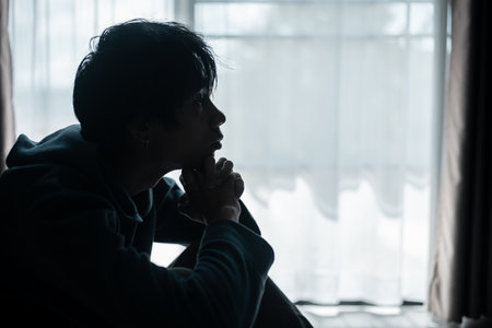 Silhouette of lost cast long shadow, embodying deep despair and hopelessness left him feeling perpetually stressed, sad, and unhappy. man sat alone, feeling weight of anxiety, stress, and depression.の写真素材