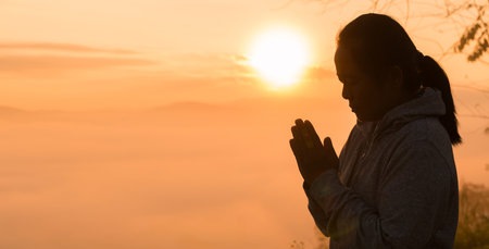 Christian woman raised her hand in worship and prayer to God, seeking peace through Jesus Christ during a serene sunrise morning. worship, christian, jesus christ, hand, god, peace, pray, sunrise.の写真素材