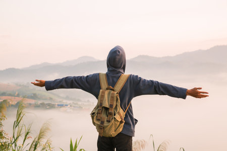 At sunrise, holiday maker embraced adventurous lifestyle of hiking through fog-covered mountains, with a backpack full of essentials and deep appreciation for beauty of nature. travel, sunrise, fog.の写真素材
