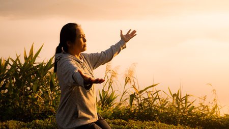 Woman in silhouette, in prayer at sunrise with sun rising in summer sky, embracing her faith amidst beauty of nature. worship, sunrise, woman, silhouette, sky, sun, nature, summer, prayer.の写真素材