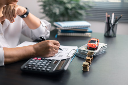 Finance and tax expense calculation at office desk with calculator, toy car, stacked coins and paperworkの写真素材
