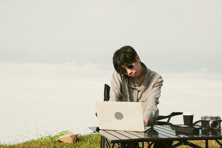 Young business man working computer on peak hill. Hiker online shopping on laptop at sunset, sunrise on top mountain, freelance person remote work with digital tablet. travel vacation holiday conceptの写真素材