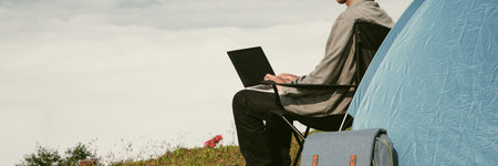 Young business man working computer on peak hill. Hiker online shopping on laptop at sunset, sunrise on top mountain, freelance person remote work with digital tablet. banner with copy spaceの写真素材