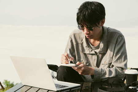 Young business man working computer on peak hill. Hiker online shopping on laptop at sunset, sunrise on top mountain, freelance person remote work with digital tablet.の写真素材