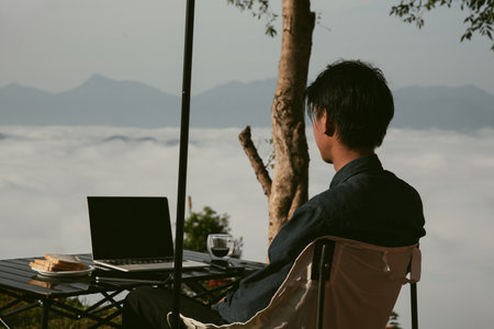 Young business man working computer on peak hill. Hiker online shopping on laptop at sunset, sunrise on top mountain, freelance person remote work with digital tablet. travel vacation holiday conceptの写真素材