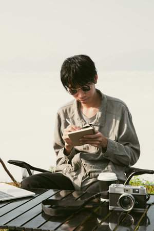 Young man working on a computer on a hill. Hiker with a laptop at sunset or sunrise on top of a mountain, freelance person remote working with a digital tablet. Travel, vacation, holiday conceptの写真素材