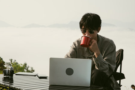 Young business man working computer on peak hill. Hiker online shopping on laptop at sunset, sunrise...