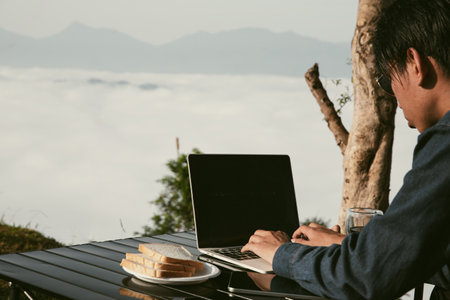 Young business man working computer on peak hill. Hiker online shopping on laptop at sunset, sunrise...