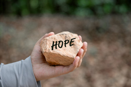 Woman hand holding stone with word hope engraved concept for faith, love, spirituality, religion. Happy female being thankful. Spiritual girl praying with hope. Positive asian young woman feeling hopeの写真素材