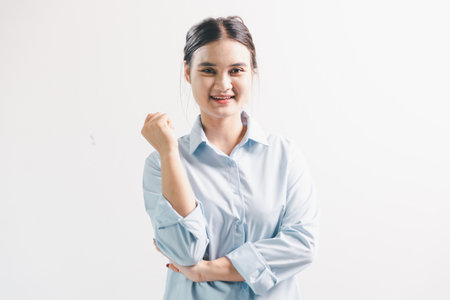 Asian woman rejoicing, looking happy, champion, fist pump gesture, standing over white background. young woman had happy, positive expression on her face, highlighted by bright smile.の写真素材