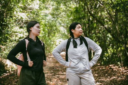 Two female friends with backpacks on vacation hiking through countryside together. Asian friend girls backpacker friend travel in forest wild together. happy and enjoying sunny day while hiking.の写真素材