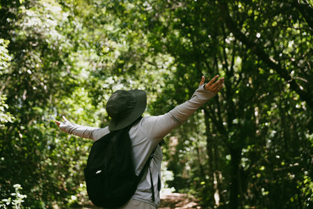 Young female traveler with backpack walking in national park or forest. recreation sport in nature. Female person bag, wave for hiking journey in woods. adventure in forest. trekking with backpackの写真素材