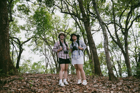 Two female friends with backpacks on vacation hiking through countryside together. Asian friend girls backpacker friend travel in forest wild together. happy and enjoying sunny day while hiking.の写真素材