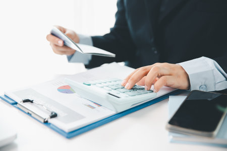 Business hands holding saving account passbook with calculator, account and saving concept. finance effectively, calculate income, track each bill and payment, accounting for bank statements and tax.の写真素材
