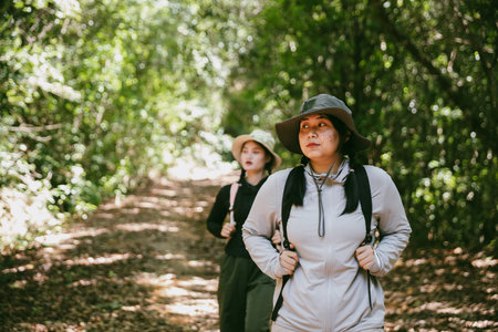 Two female friends with backpacks on vacation hiking through countryside together. Asian friend...