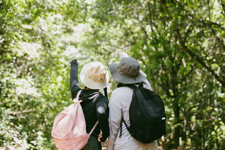Two female friends with backpacks on vacation hiking through countryside together. Asian friend girls backpacker friend travel in forest wild together. happy and enjoying sunny day while hiking.の写真素材