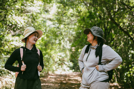 Two female friends with backpacks on vacation hiking through countryside together. Asian friend girls backpacker friend travel in forest wild together. happy and enjoying sunny day while hiking.の写真素材