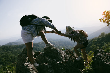 Two friends helping with teamwork trying to reach top of mountains during wonderful summer sunset. Teamwork couple hiking help each other trust assistance. Team of climbers two friends hiker.の写真素材