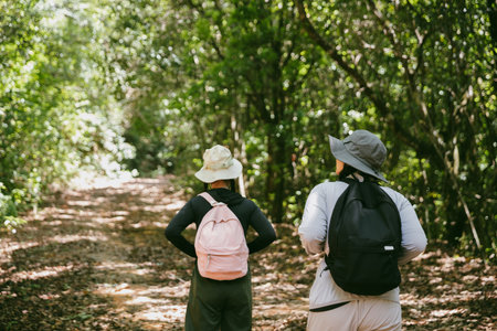 Two female friends with backpacks on vacation hiking through countryside together. Asian friend girls backpacker friend travel in forest wild together. happy and enjoying sunny day while hiking.の写真素材