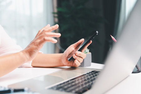 Close-up shot, woman sits at a wooden table using her smartphone, with her finger touching the phone screen as she navigates mobile banking, online shopping, and social media networks.の写真素材