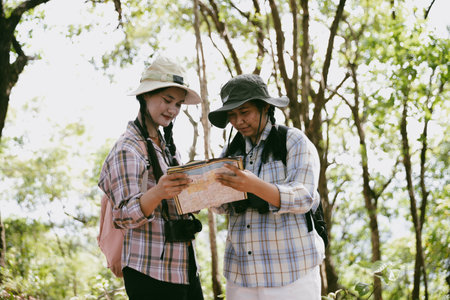 Two female friends with backpacks on vacation hiking through countryside together. Asian friend girls backpacker friend travel in forest wild together. happy and enjoying sunny day while hiking.の写真素材