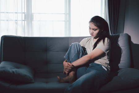Depression woman sit on sofa. Despair sorrow person sitting alone and hugging knees, Boring sad upset frustrated stressed. struggling to find hope amid suffocating burden. mental health concept.の写真素材