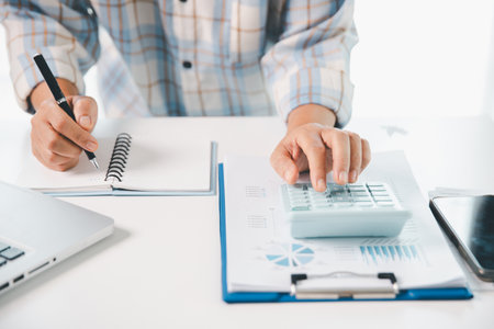 Accountant working on desk using calculator for calculate finance report in office. business finance, calculate tax by organizing financial documents, tracking income investment, accounting by hand.の写真素材