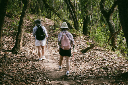 Two female friends with backpacks on vacation hiking through countryside together. Asian friend girls backpacker friend travel in forest wild together. happy and enjoying sunny day while hiking.の写真素材