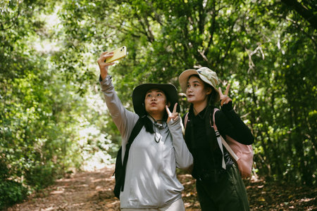 Two female friends with backpacks on vacation hiking through countryside together. Asian friend girls backpacker friend travel in forest wild together. happy and enjoying sunny day while hiking.の写真素材