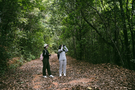Two female friends with backpacks on vacation hiking through countryside together. Asian friend girls backpacker friend travel in forest wild together. happy and enjoying sunny day while hiking.の写真素材