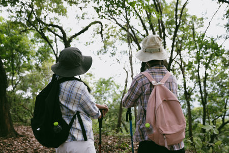 Two female friends with backpacks on vacation hiking through countryside together. Asian friend girls backpacker friend travel in forest wild together. happy and enjoying sunny day while hiking.の写真素材