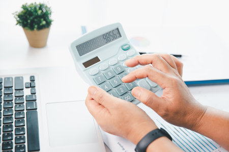 Accountant working on desk using calculator for calculate finance report in office. business finance, calculate tax by organizing financial documents, tracking income investment, accounting by hand.の写真素材