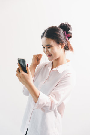 Asian woman rejoicing, looking happy, fist pump gesture, standing over white background. young woman had happy, positive expression on her face, highlighted by bright smile.の写真素材