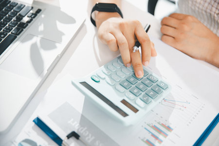 Accountant working on desk using calculator for calculate finance report in office. business finance, calculate tax by organizing financial documents, tracking income investment, accounting by hand.の写真素材