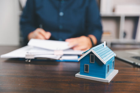 House model placed on table alongside coins, paperwork symbolizes real estate investment, property valuation, representing financial planning, mortgage options, market analysis in property business.の写真素材