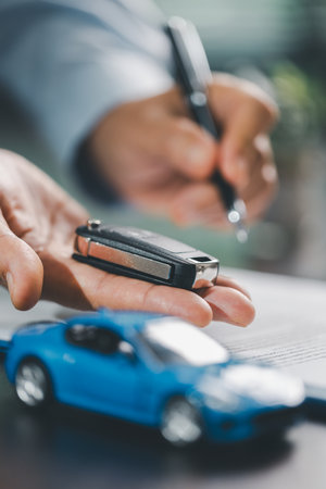 Business office, woman employee finalizes deal with client, handing over car key after signing contract and reviewing insurance and loan documents for sale or rent of vehicle at table.の写真素材