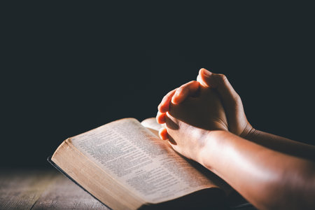 Hands clasped in prayer over the holy Bible, the faithful Christian worships God in church, holding onto hope and belief, guided by religion and a deep commitment to their religious faith.の写真素材