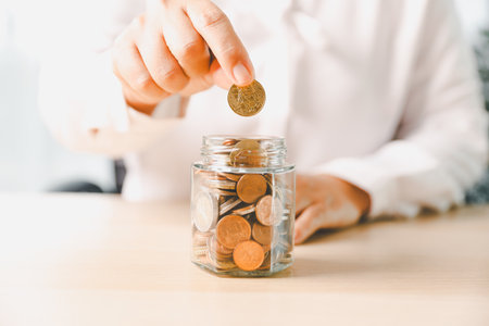 Hand places coin into saving jar, representing how smart finance, investment, banking practices turn...
