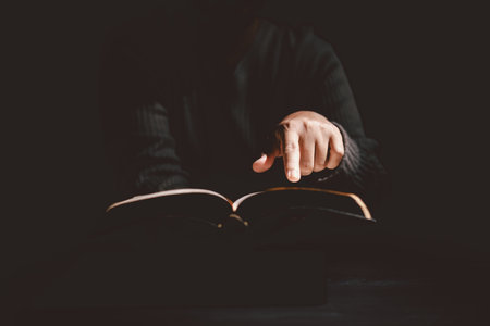 Hands holding and offering the Holy Bible with dramatic light in darkness, symbolizing Christianity,...